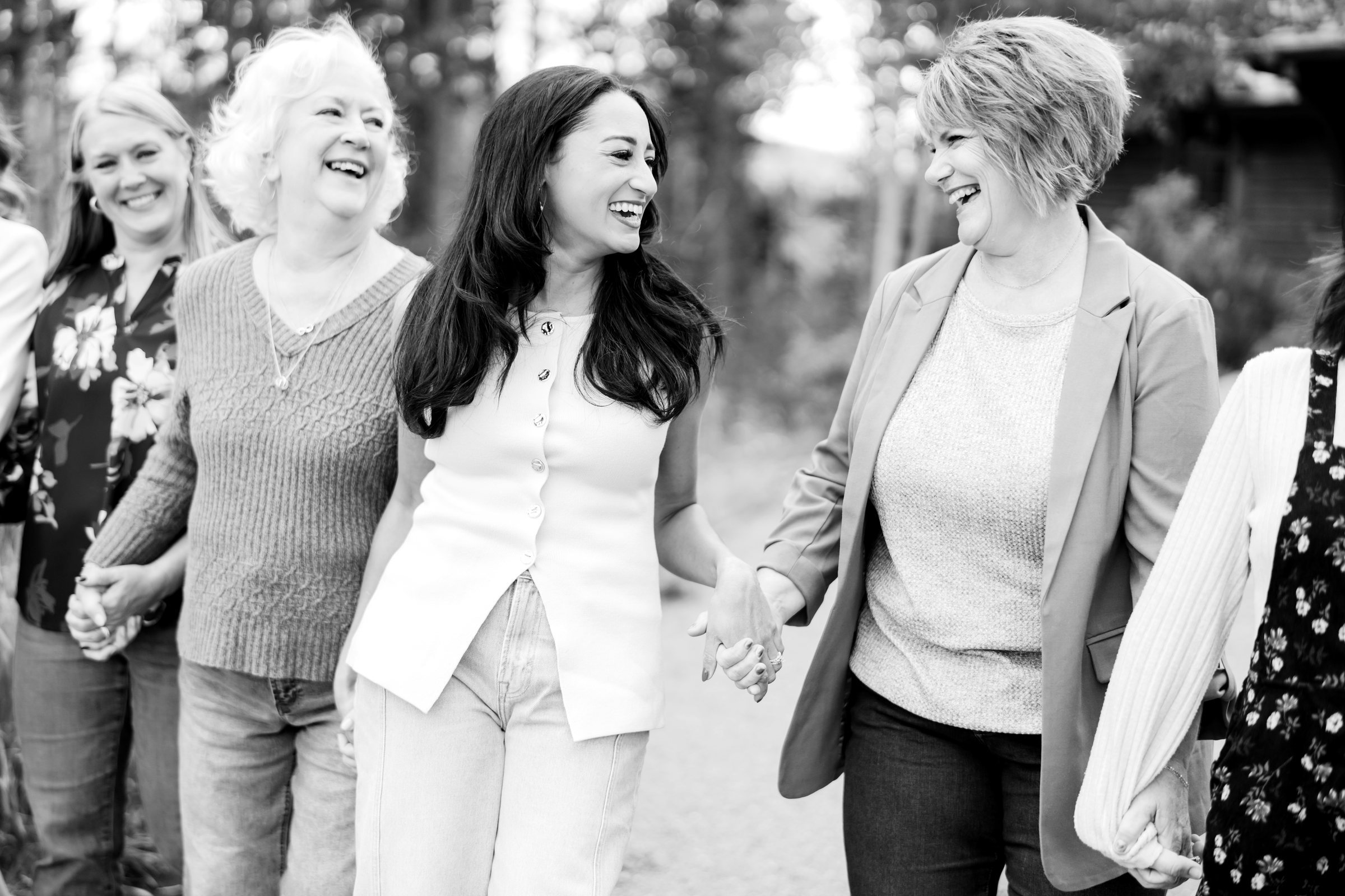 Four women walking hand in hand along a mountain path, laughing