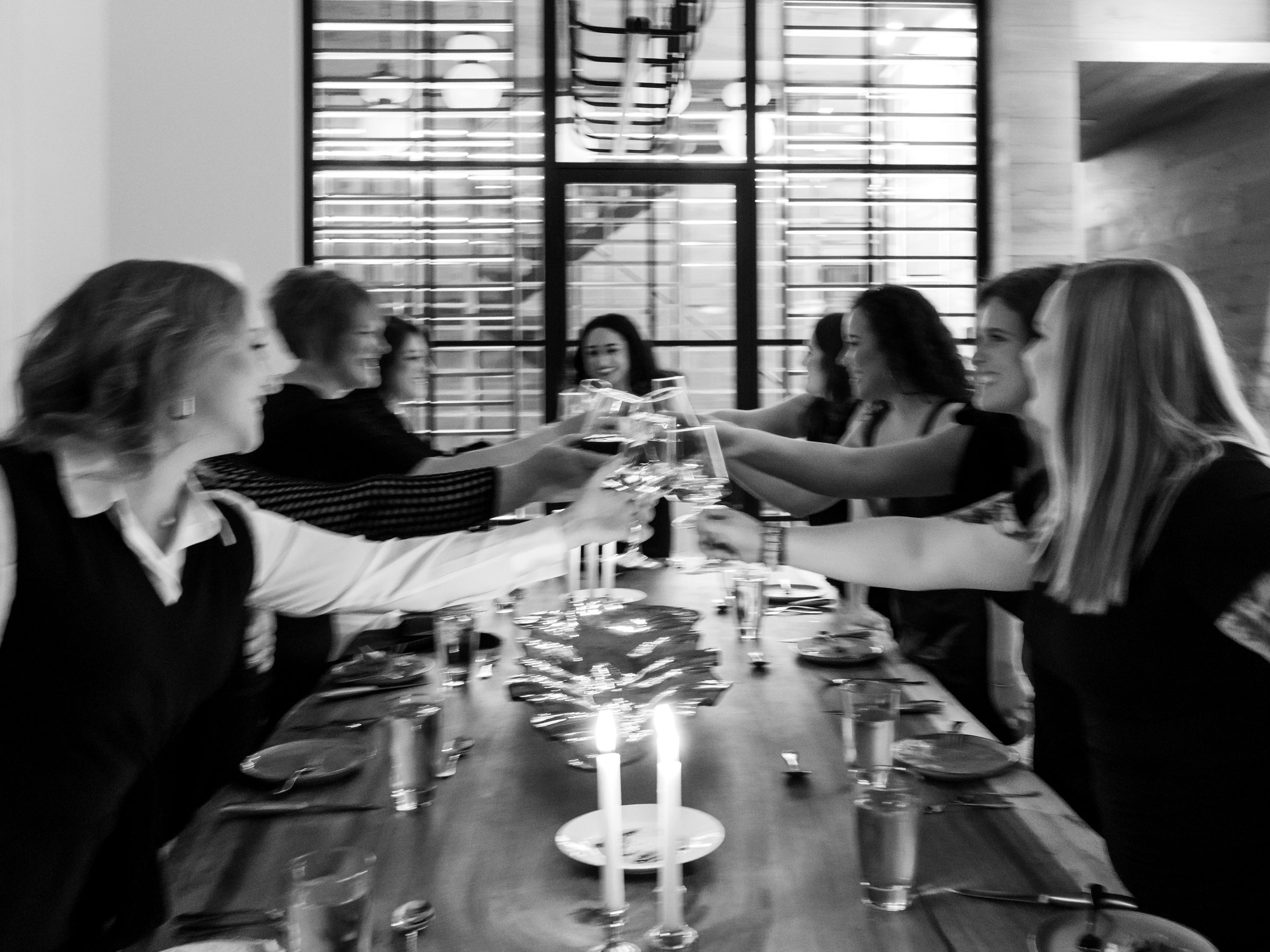Candlelit dinner table, glasses raised across the table in a toast