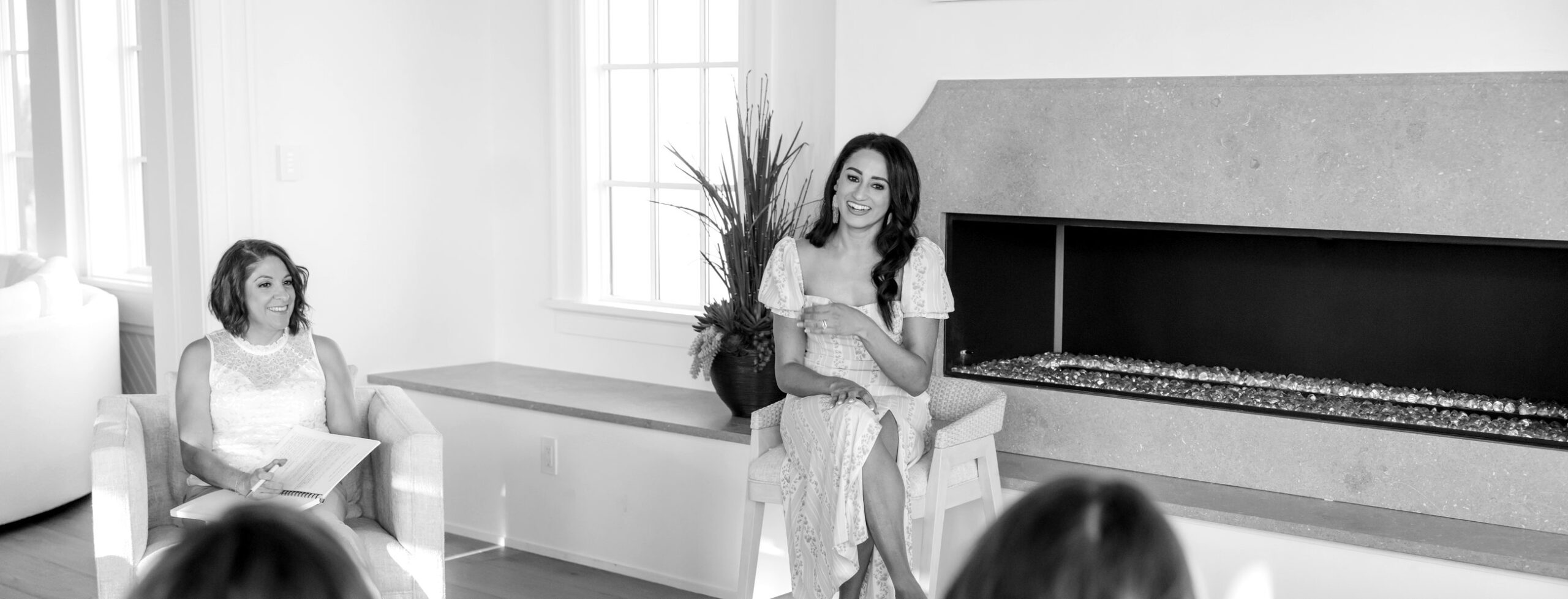 Macie Renae coaching a room of women from a stool beside the fireplace