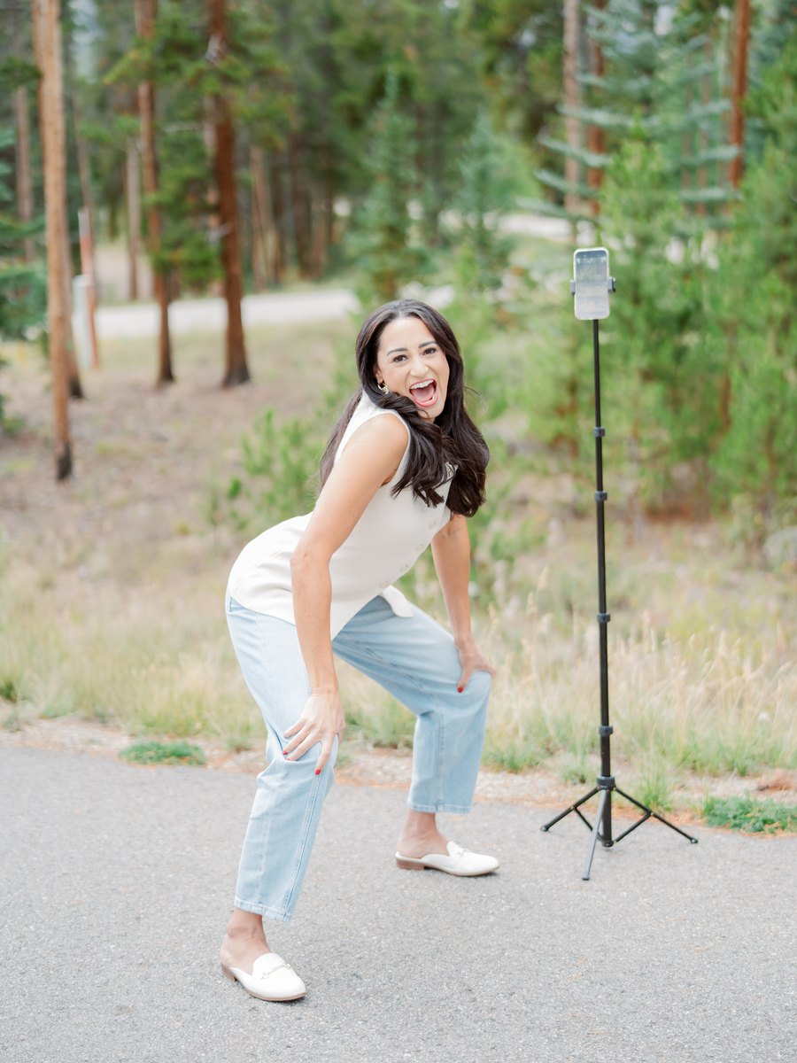 Macie Renae doubled over laughing beside a phone tripod on a mountain road