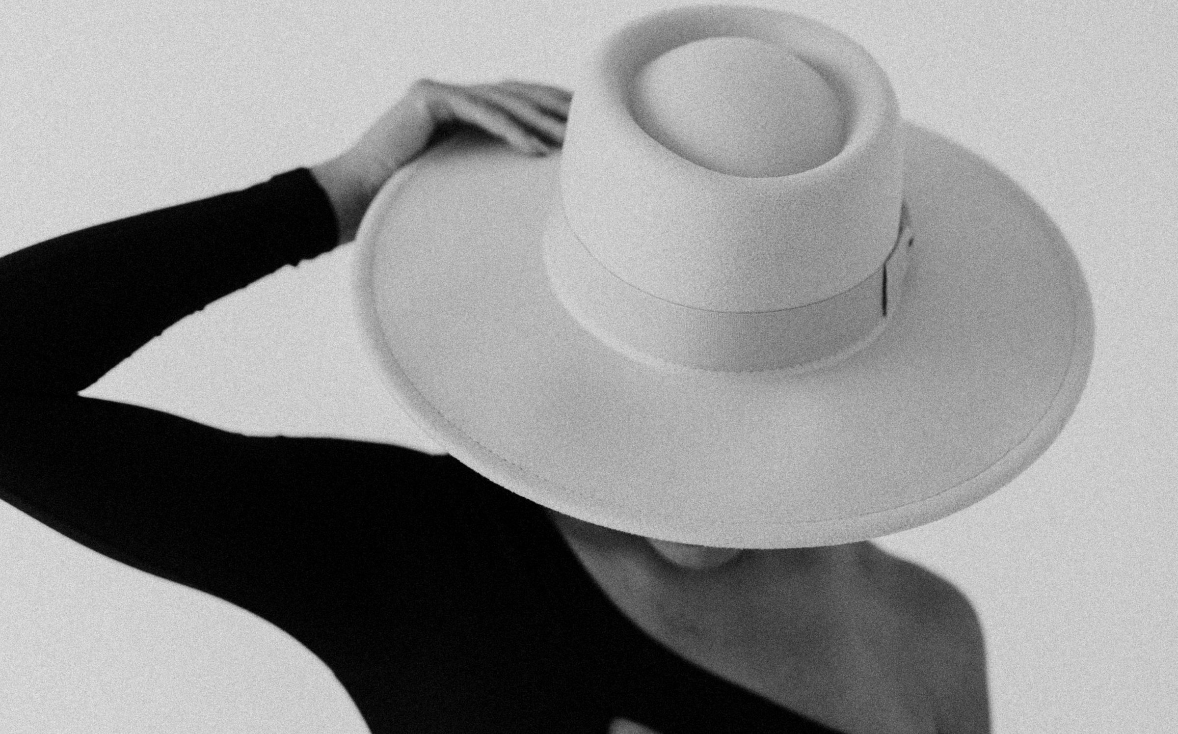 Black and white detail of a hand resting on the brim of a wide hat