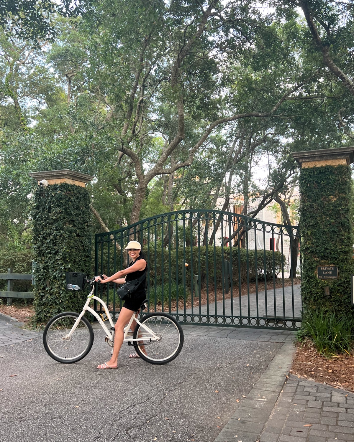 A woman on a beach cruiser bicycle at an ivy-covered gate in Alys Beach