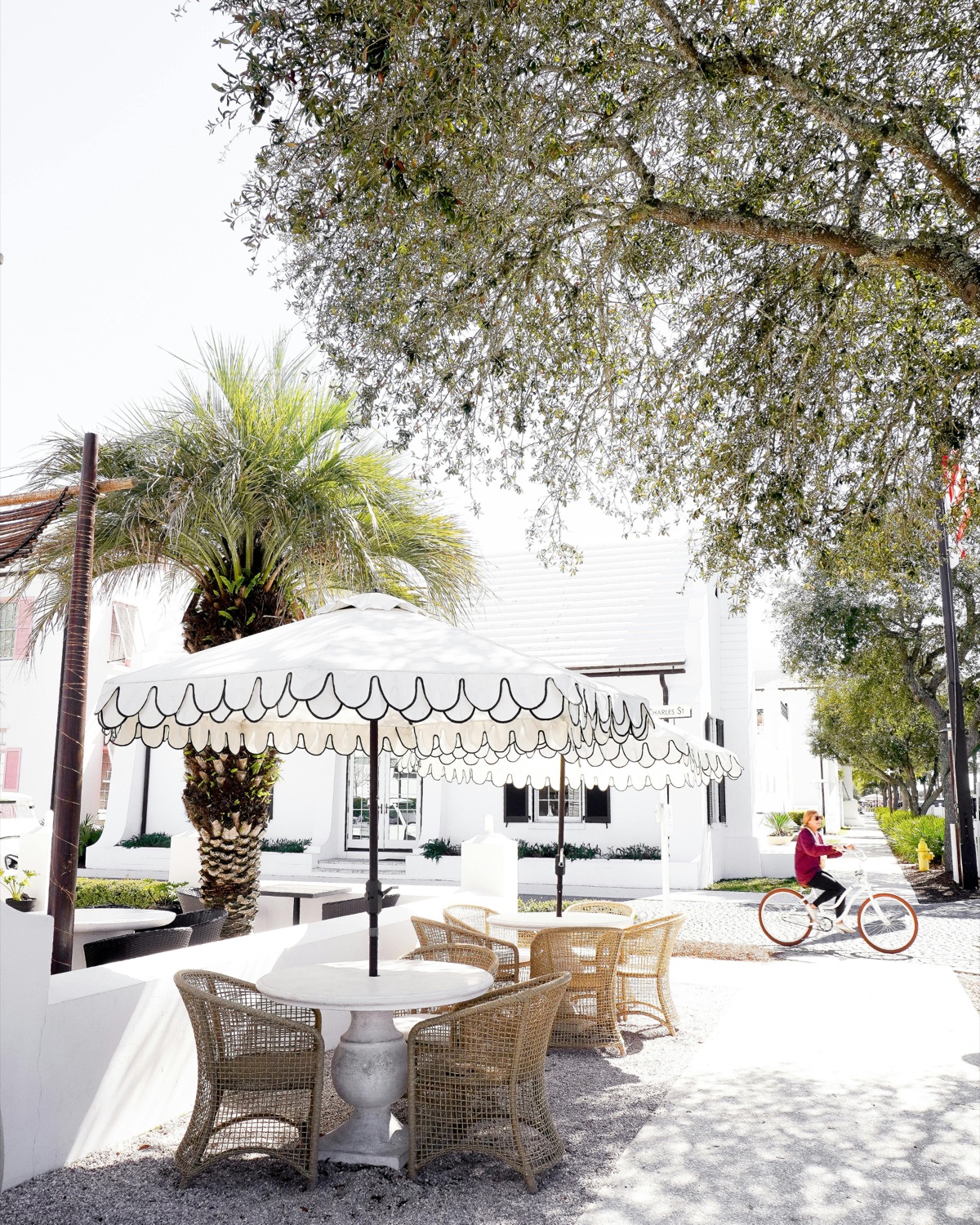 White stucco buildings, palms and cafe tables under an awning in Alys Beach
