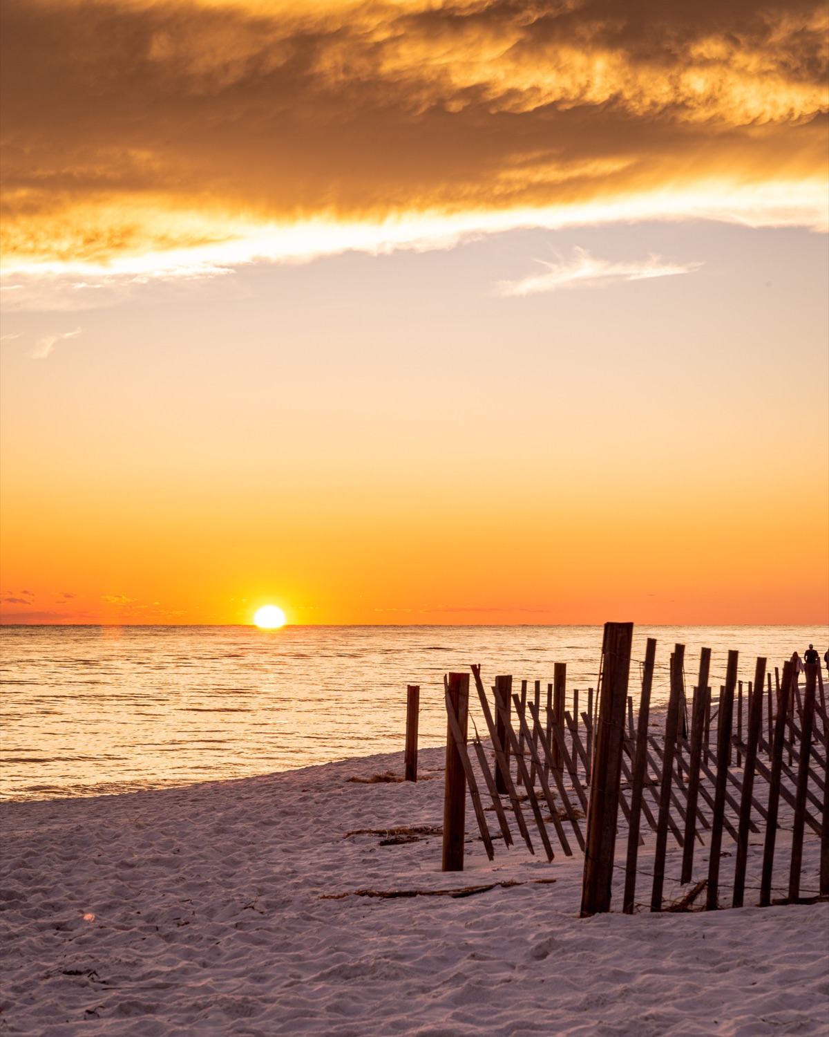 The sun setting over the Gulf behind a weathered beach fence on 30A
