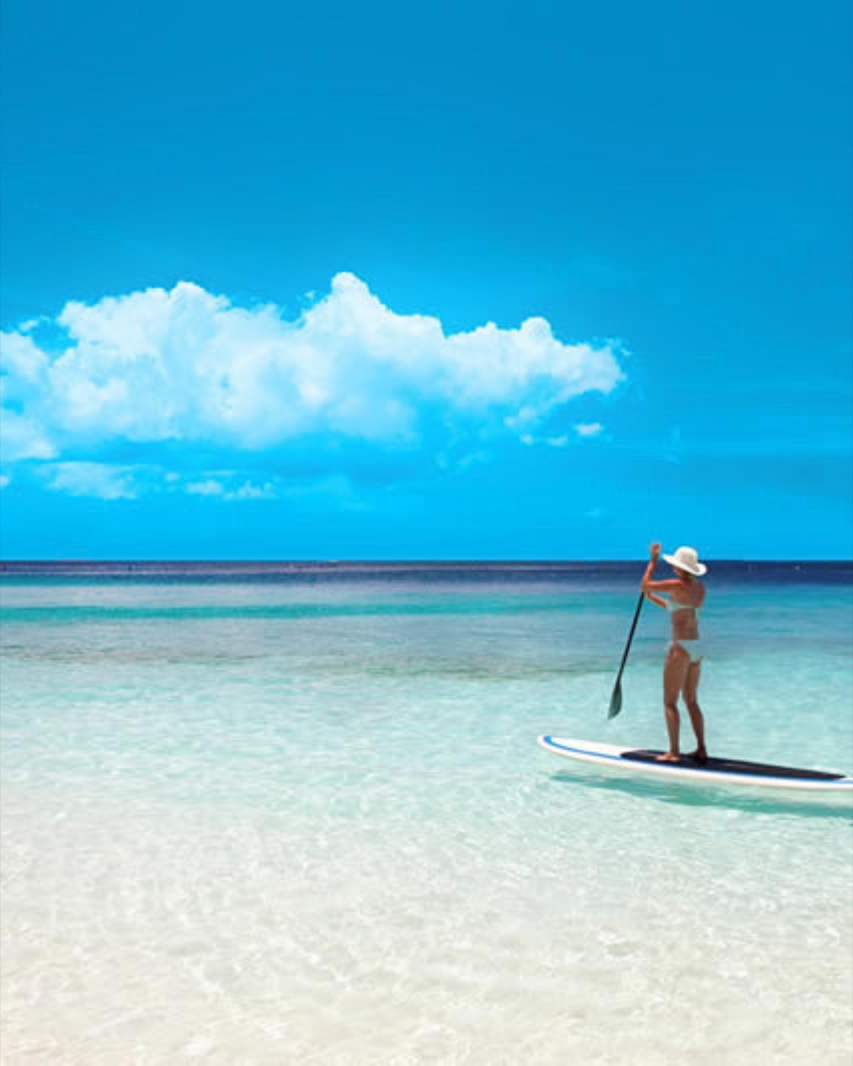 A woman paddleboarding on the clear turquoise water of the Gulf